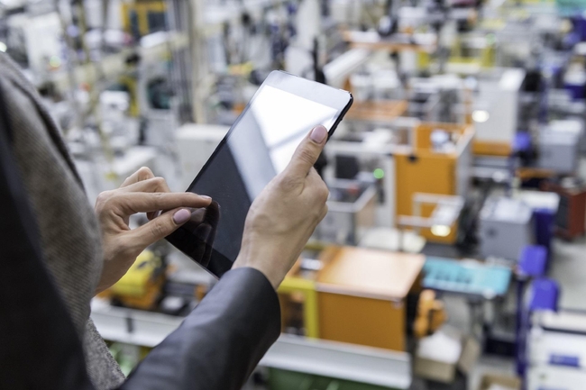 Mensch arbeitet an einem Tablet in einer Fabrikhalle